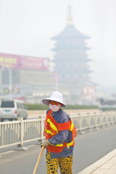近日，在古都洛陽，環(huán)衛(wèi)工人身后的“天堂”被霧霾籠罩著。