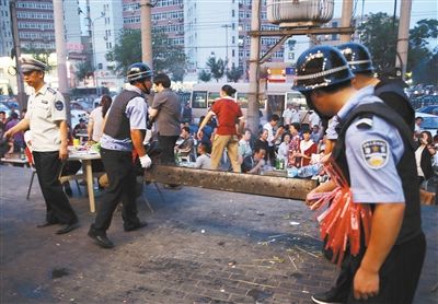 6月13日晚8點，朝陽路和青年路交叉口西側(cè)，一次聯(lián)合執(zhí)法行動中，輔警與協(xié)管抬走商戶的燒烤用具。新京報記者 尹亞飛 攝