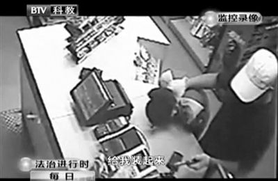 戴帽男子一手掐住加油站營業(yè)員，一手持發(fā)令槍指向另一營業(yè)員，要求“把錢給我裝起來”。