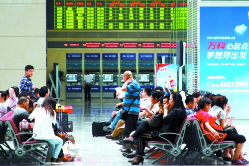 候車大廳溫度很高，一名乘客一手扇風(fēng)、一手擦汗