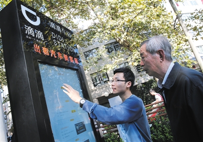 10月15日，滴滴工作人員（左）指導(dǎo)乘客使用“滴滴車站”的電子屏預(yù)約出租車。