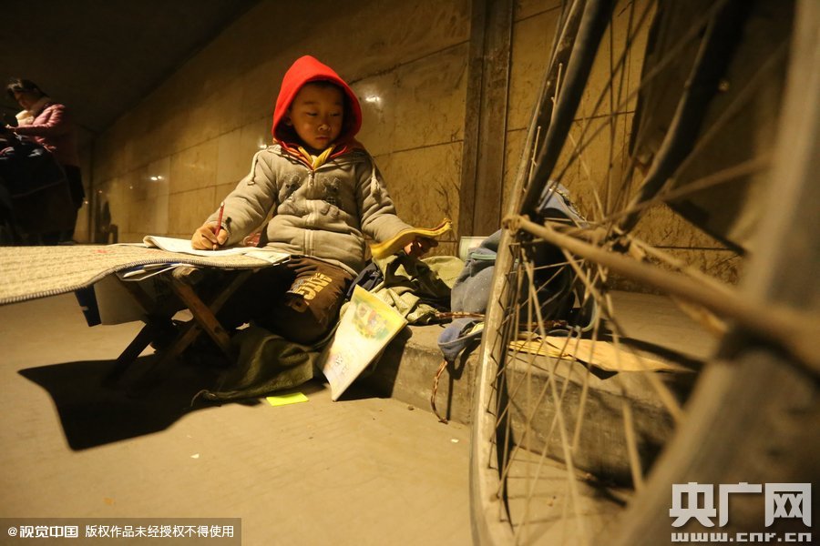 2015年11月8日晚，鄭州，7歲男孩涵洞橋下陪父母練攤，路邊燈下坐小馬扎上寫作業(yè)。