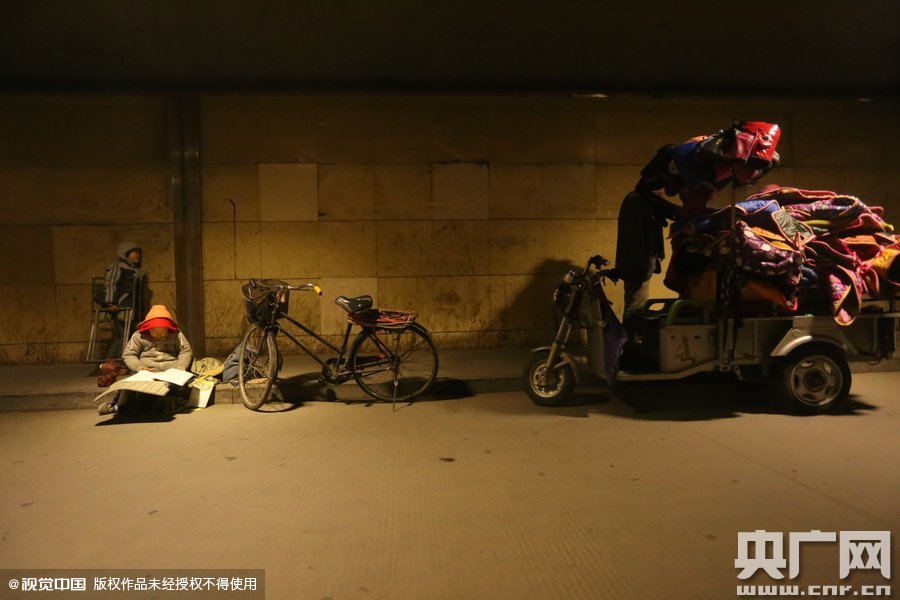 2015年11月8日晚，鄭州，7歲男孩涵洞橋下陪父母練攤，路邊燈下坐小馬扎上寫作業(yè)。