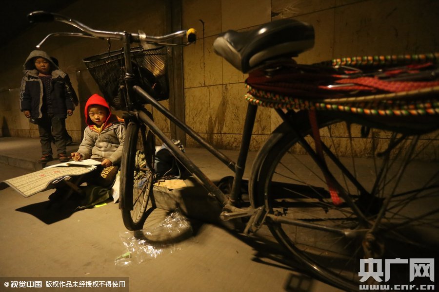 2015年11月8日晚，鄭州，7歲男孩涵洞橋下陪父母練攤，路邊燈下坐小馬扎上寫作業(yè)。